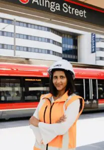 Woman of average height standing above sign that says 'alinga street', behind her is a tram about to depart