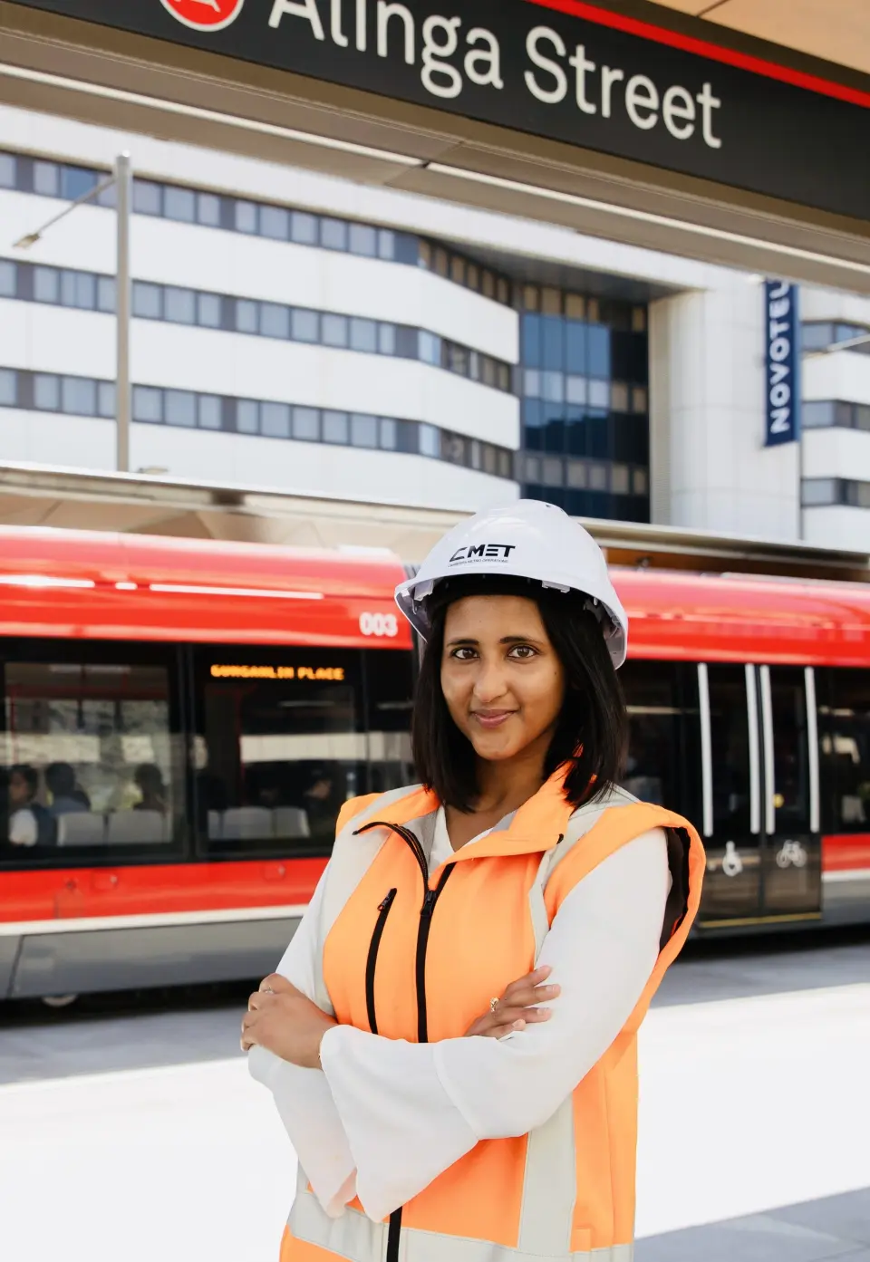 Woman of average height standing above sign that says 'alinga street', behind her is a tram about to depart